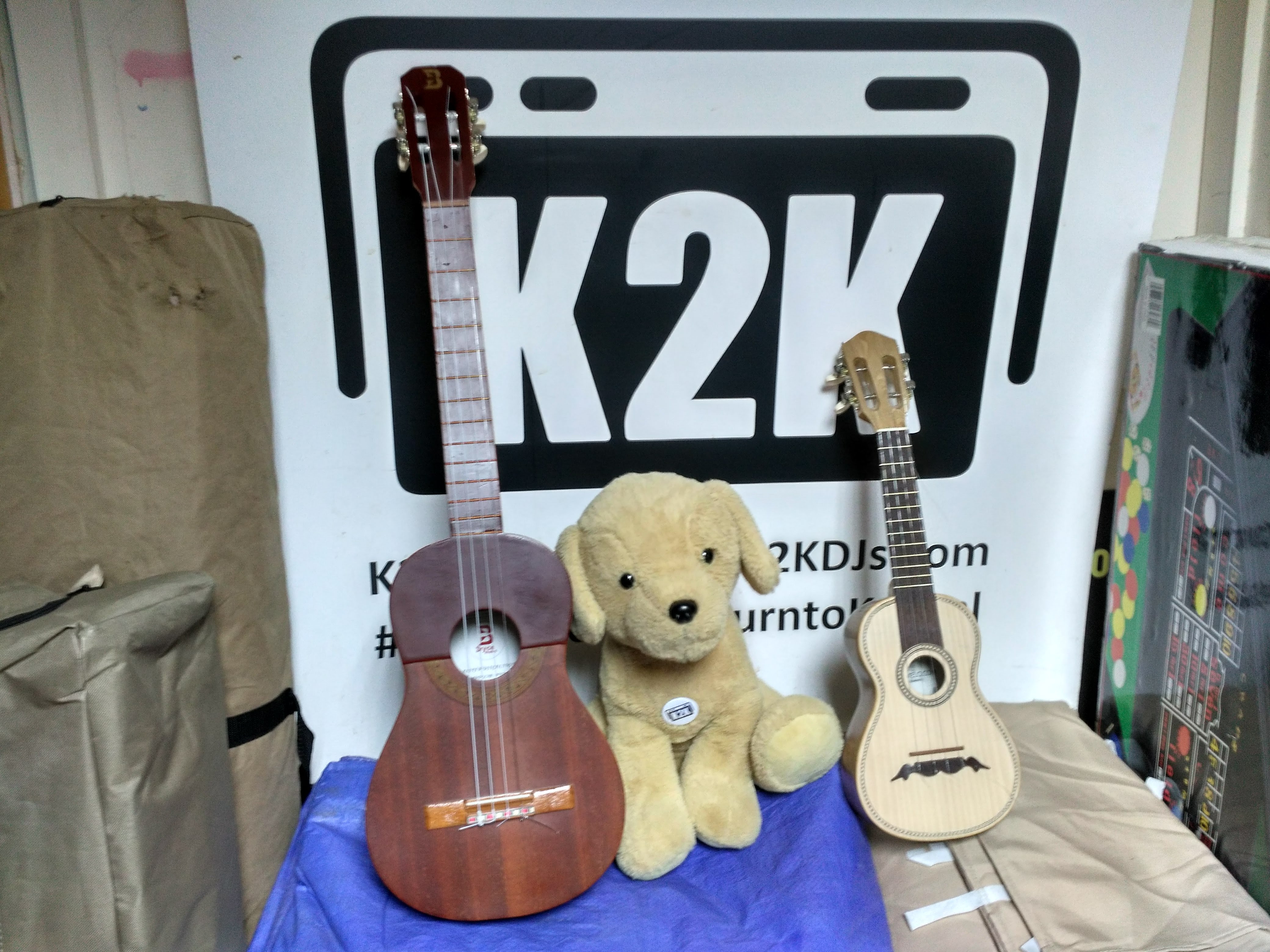 K2K Radio logo, with the K2K mascot between two instruments - a Venezuelan cuatro and a Portuguese cavaquinho