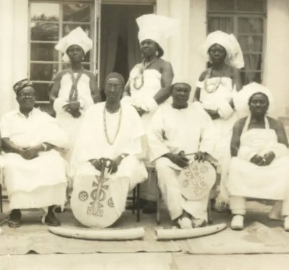 The Obi of Onitsha with Otu-Odu women in 1935, wearing elaborate, voluminous Ichafu fashioned from stiffened Akwa Ocha to create a sculptural, high-status Silhouette
