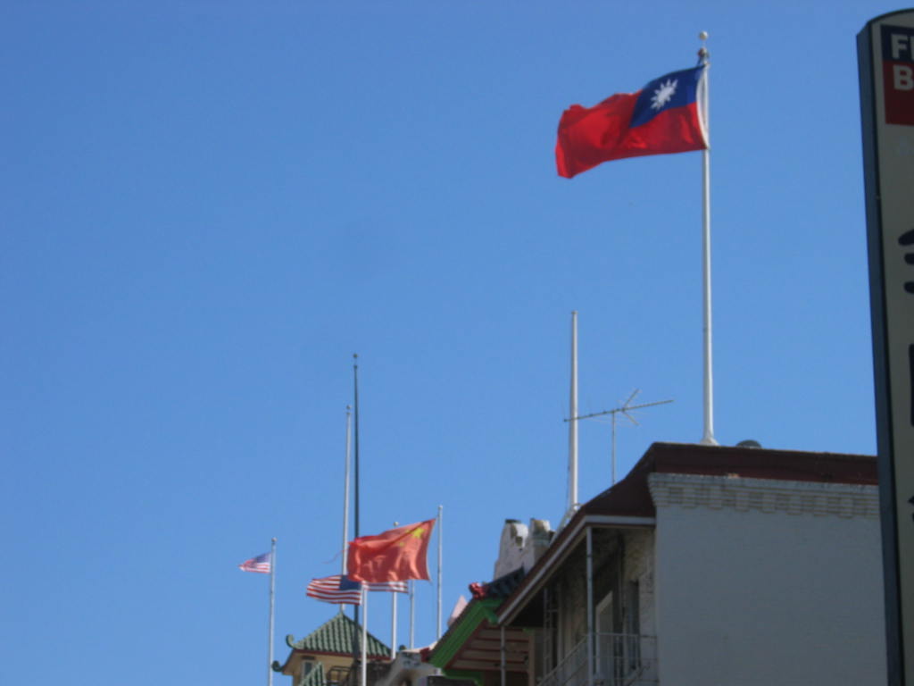 Flags of the Republic of China (foreground), People's Republic of China (middleground), and United States (background) can be seen flying atop adjacent buildings in San Francisco Chinatown. Most benevolent associations in San Francisco continue to fly the flag of the Republic of China due to their close relations with the KMT.