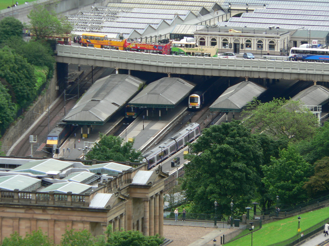 Lothian tour buses (L-R): Mac Tours, Majestic Tour, City Sightseeing and Edinburgh Tour, on Waverley Bridge. Also, an Airlinks bus far right, and Waverley station below