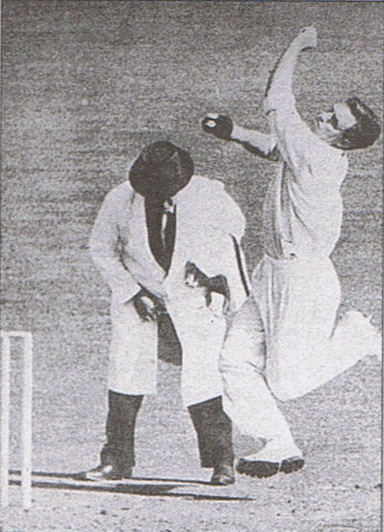 An umpire checks Lindwall's feet for a no-ball.