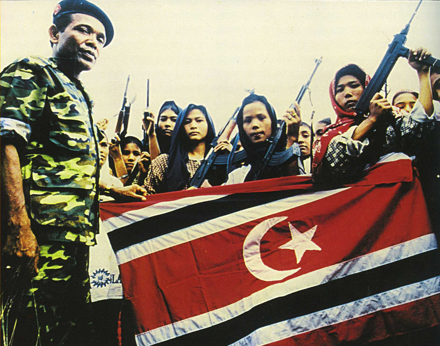 GAM commander, Abdullah Syafi'i, with female soldiers holding the Aceh (GAM) flag, during the insurgency in Aceh, 1999.