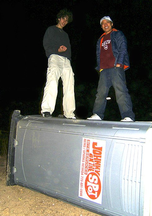 Two pranksters standing over a fallen portable toilet