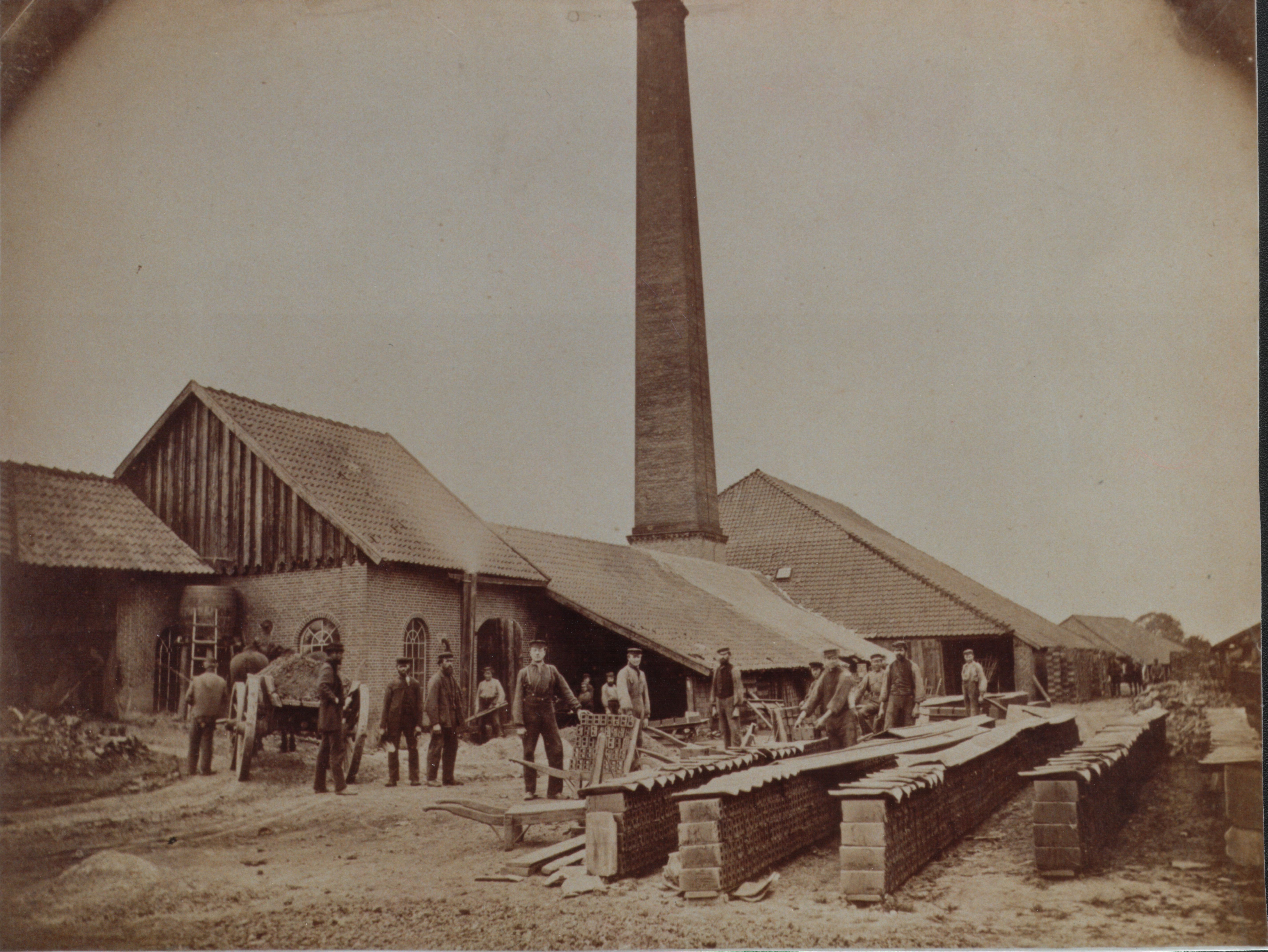 Men working in the yard of a brickworks in Germany, the tall chimney of the kiln visible, 1890